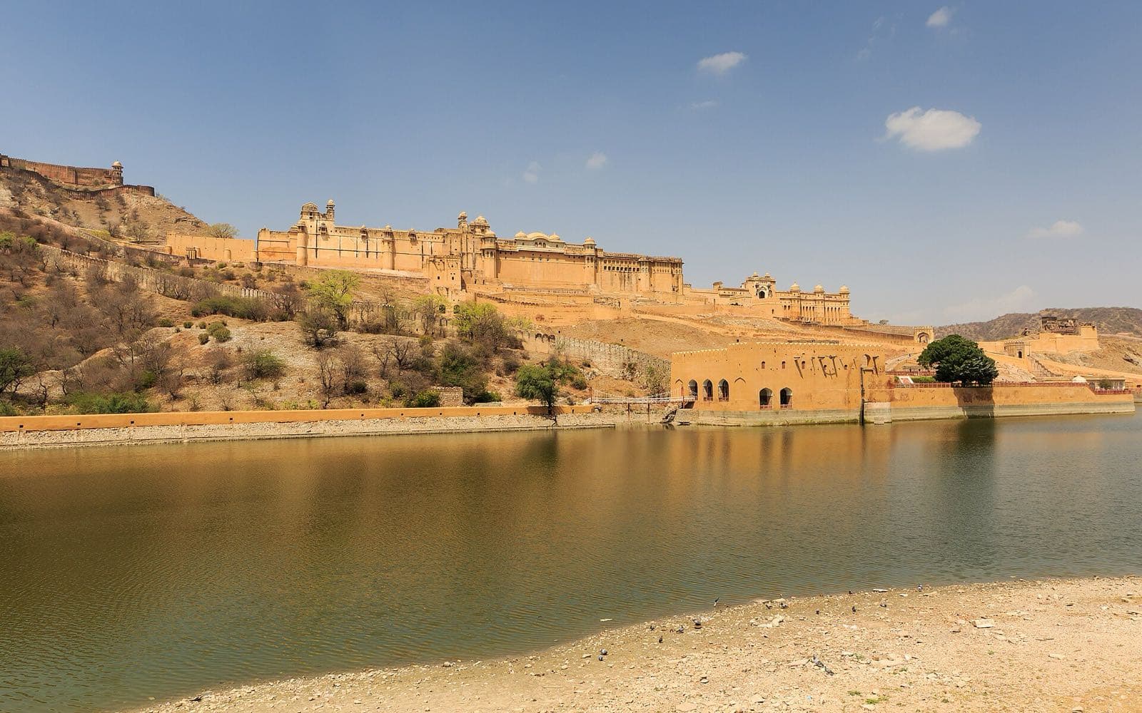 Amer Fort on its hillside above a lake, its walls reflected in the water.
