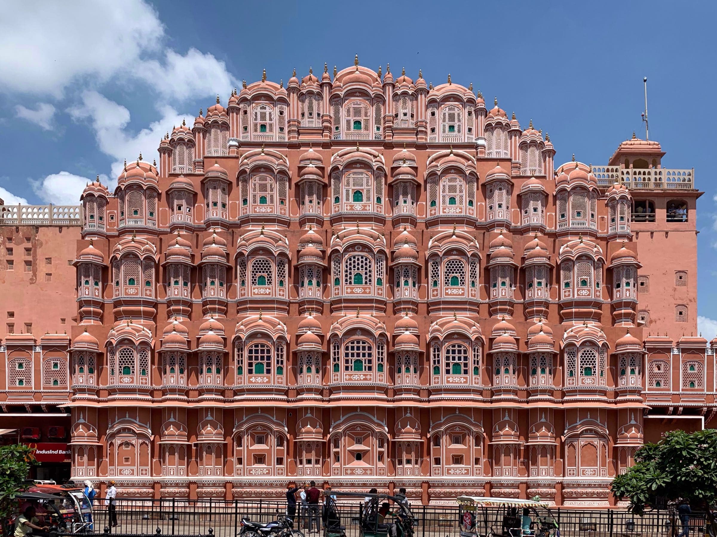 The pink sandstone façade of the Hawa Mahal in Jaipur, rising in tiers of latticed windows against a blue sky.