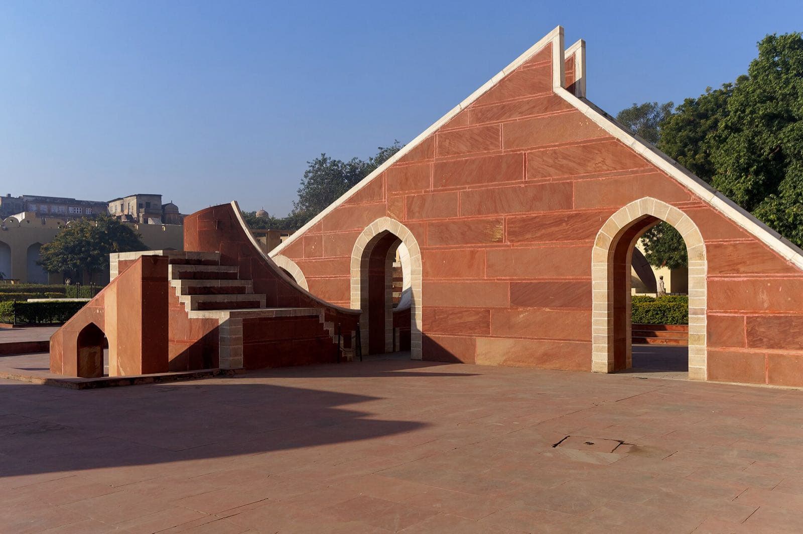 Large red sandstone instruments with arched openings and stairways at the Jantar Mantar observatory.