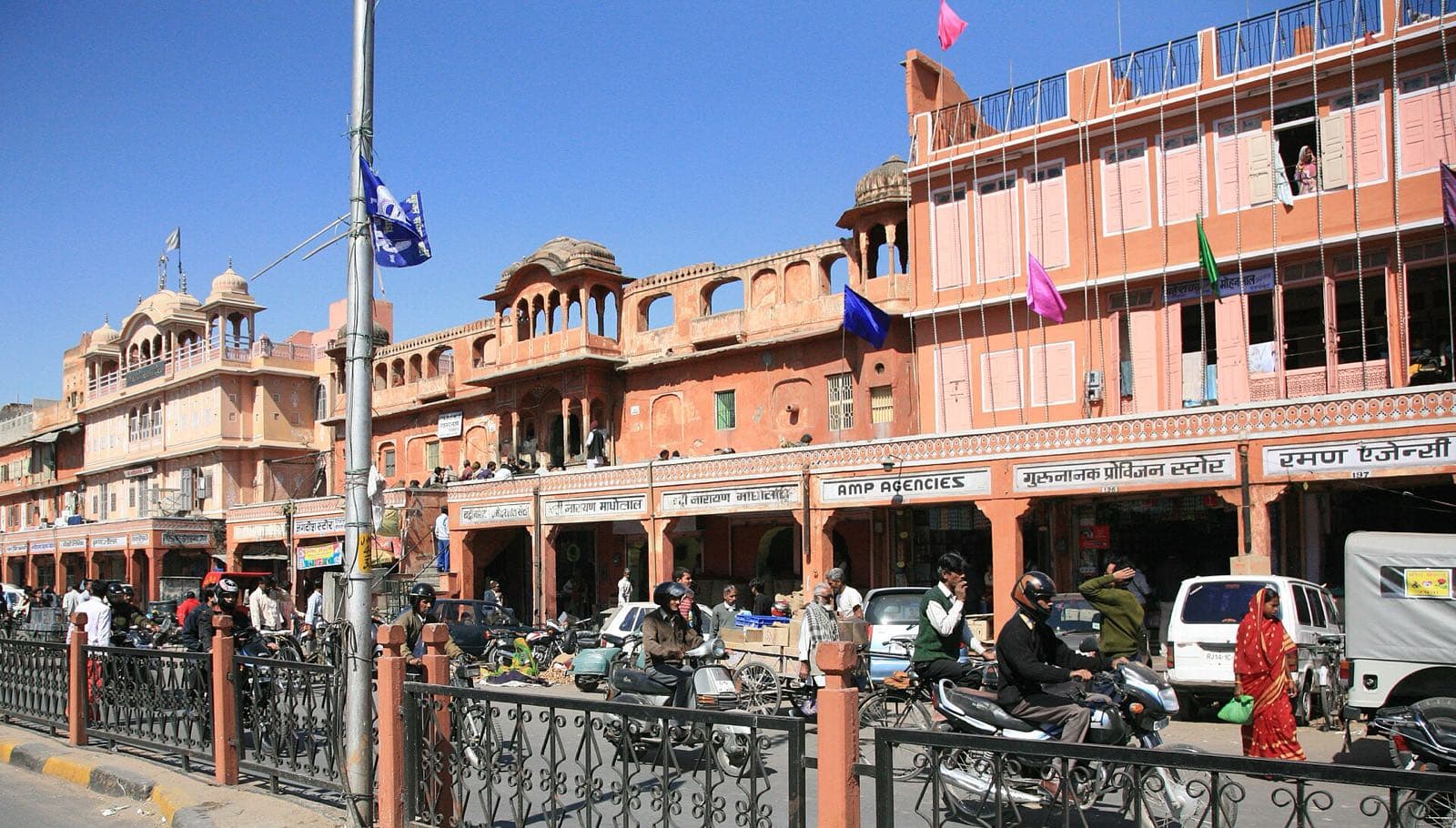 A row of pink-painted shopfronts and balconies on a busy street in Tripolia Bazaar, with scooters and shoppers below.